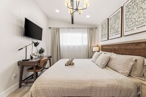 Ein Hotelzimmer mit Bett, Schreibtisch, Fernseher und einem Kunstwerk an der Wand.