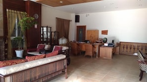 Uma sala de estar ampla, com um sofá, uma mesa de jantar e uma mesa de centro. Há uma planta em vaso e um armário de madeira.