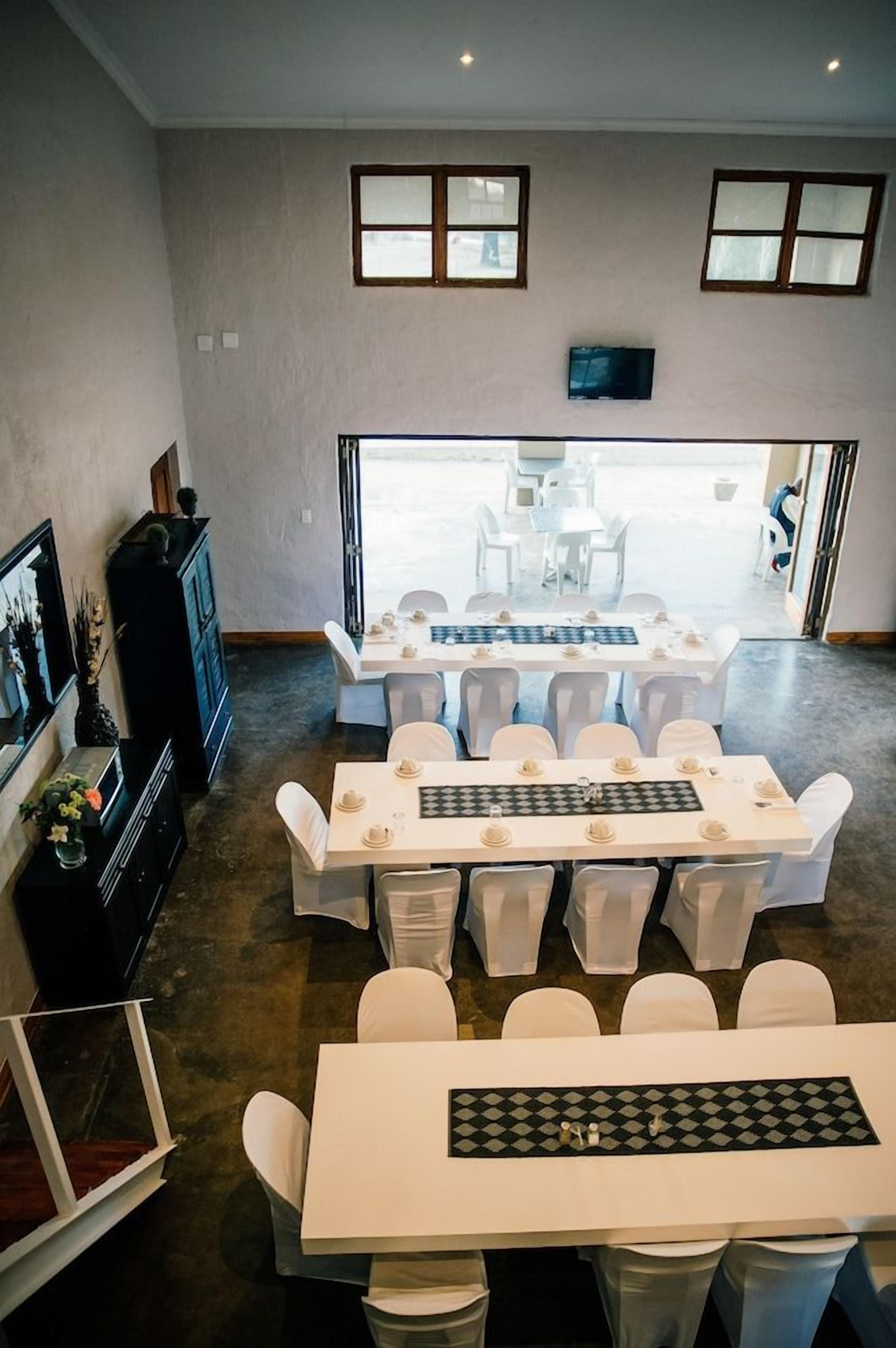 A dining area with multiple tables and chairs, a television mounted on the wall, and a view of the outdoors.