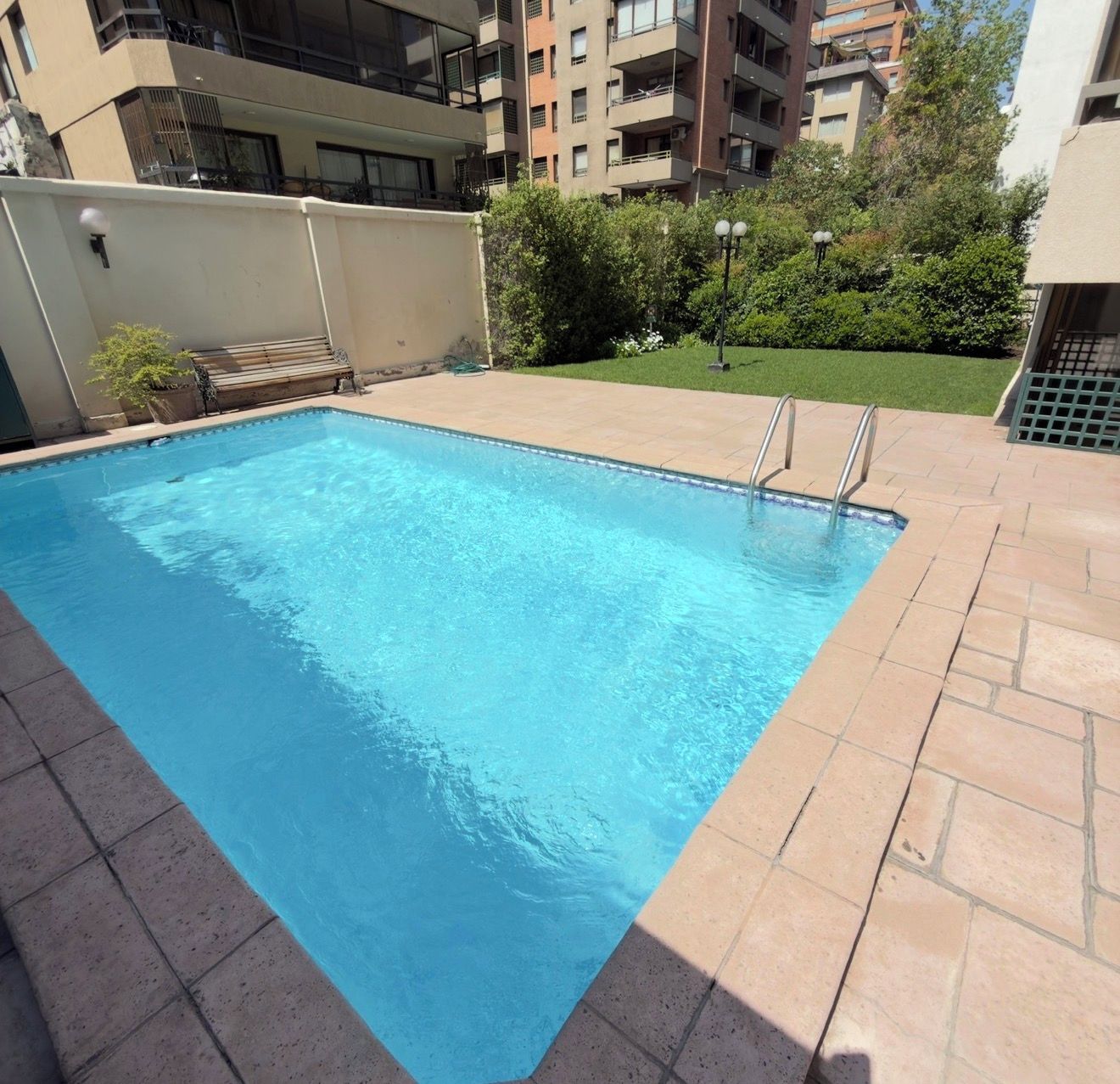 Una piscina rectangular con borde de azulejos, rodeada por un solárium empedrado.