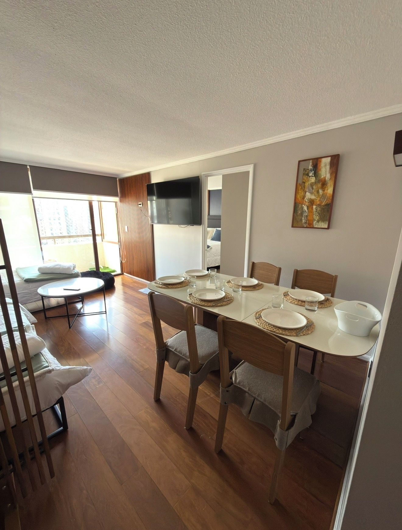 Un comedor con una mesa dispuesta para cuatro, sillas de madera y un televisor montado en la pared.
