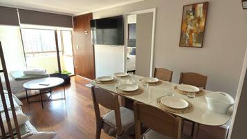 Un comedor con una mesa dispuesta para cuatro, sillas de madera y un televisor montado en la pared.