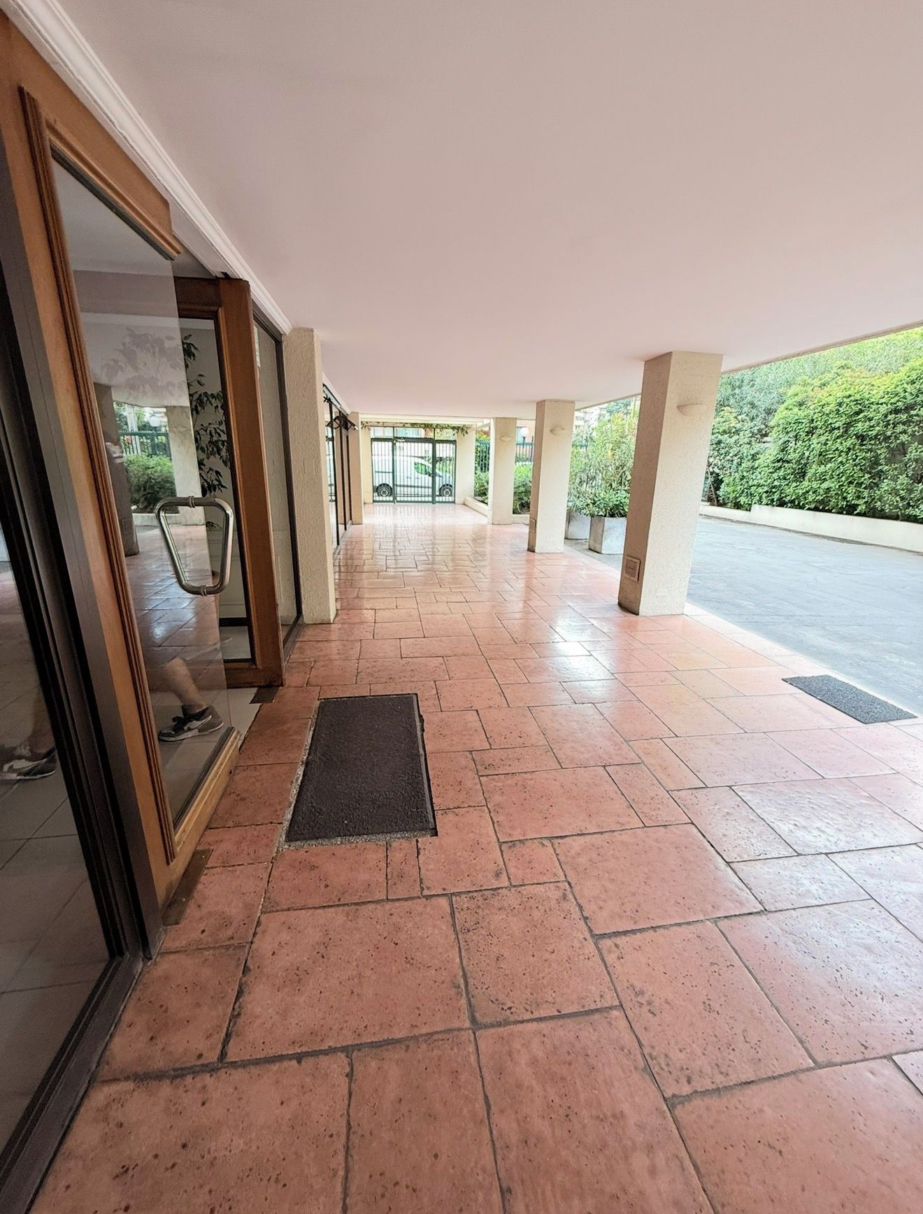 An indoor corridor with tiled flooring, a glass door entrance, and a view of a green outdoor area.