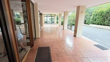 An indoor corridor with tiled flooring, a glass door entrance, and a view of a green outdoor area.