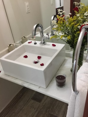 A bathroom with a white sink, a mirror, a flower vase, and a candle. - Pousada Waikiki (Tibau do Sul)