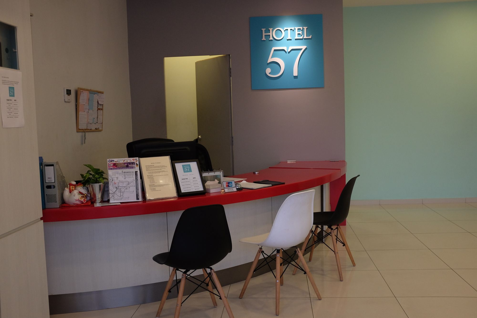 A hotel reception desk with a sign reading 'HOTEL 57', a computer, a plant, and two chairs.