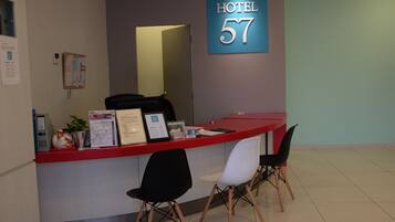 A hotel reception desk with a sign reading 'HOTEL 57', a computer, a plant, and two chairs.
