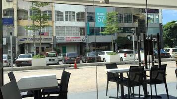 An outdoor seating area with tables and chairs, a view of the street with parked cars, and a hotel sign in the background.