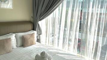 A hotel room with a large bed, a headboard, a window with sheer curtains, and a view of the outside.