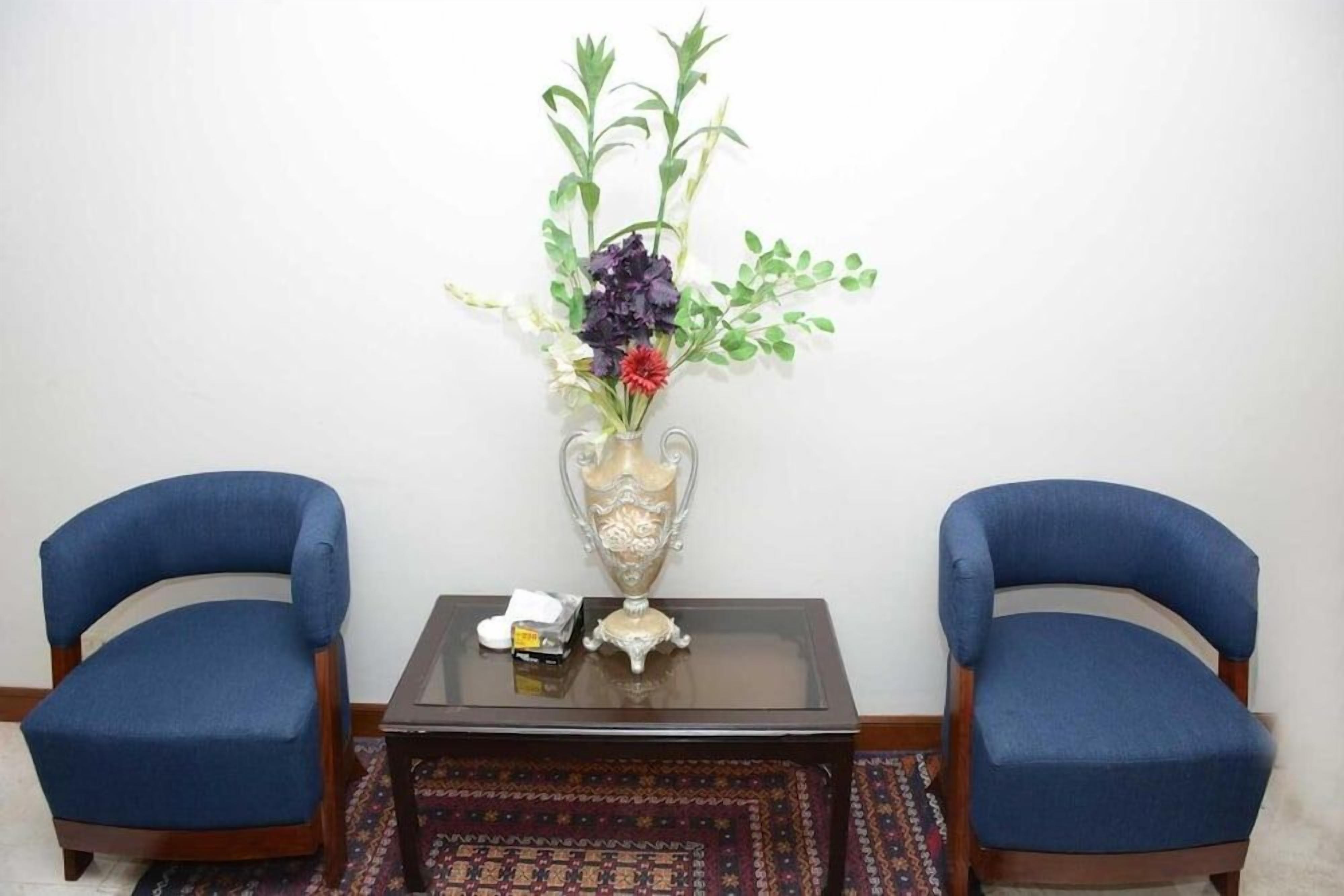 Zwei blau gepolsterte Sessel, ein kleiner Tisch mit einer Blumenvase und ein dekoratives Objekt darauf.