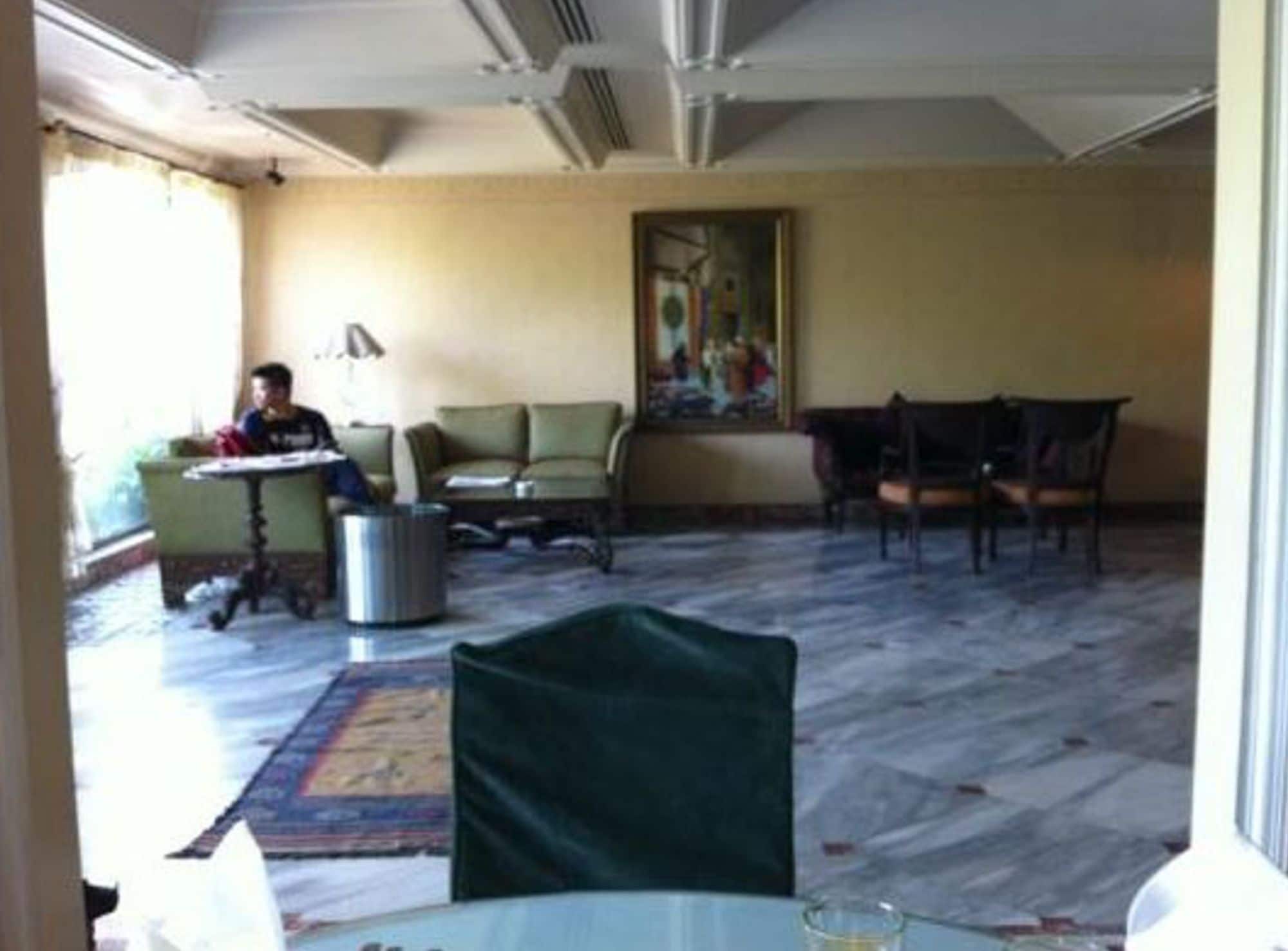 A hotel room with a dining area, a green chair, a table, and a painting on the wall.