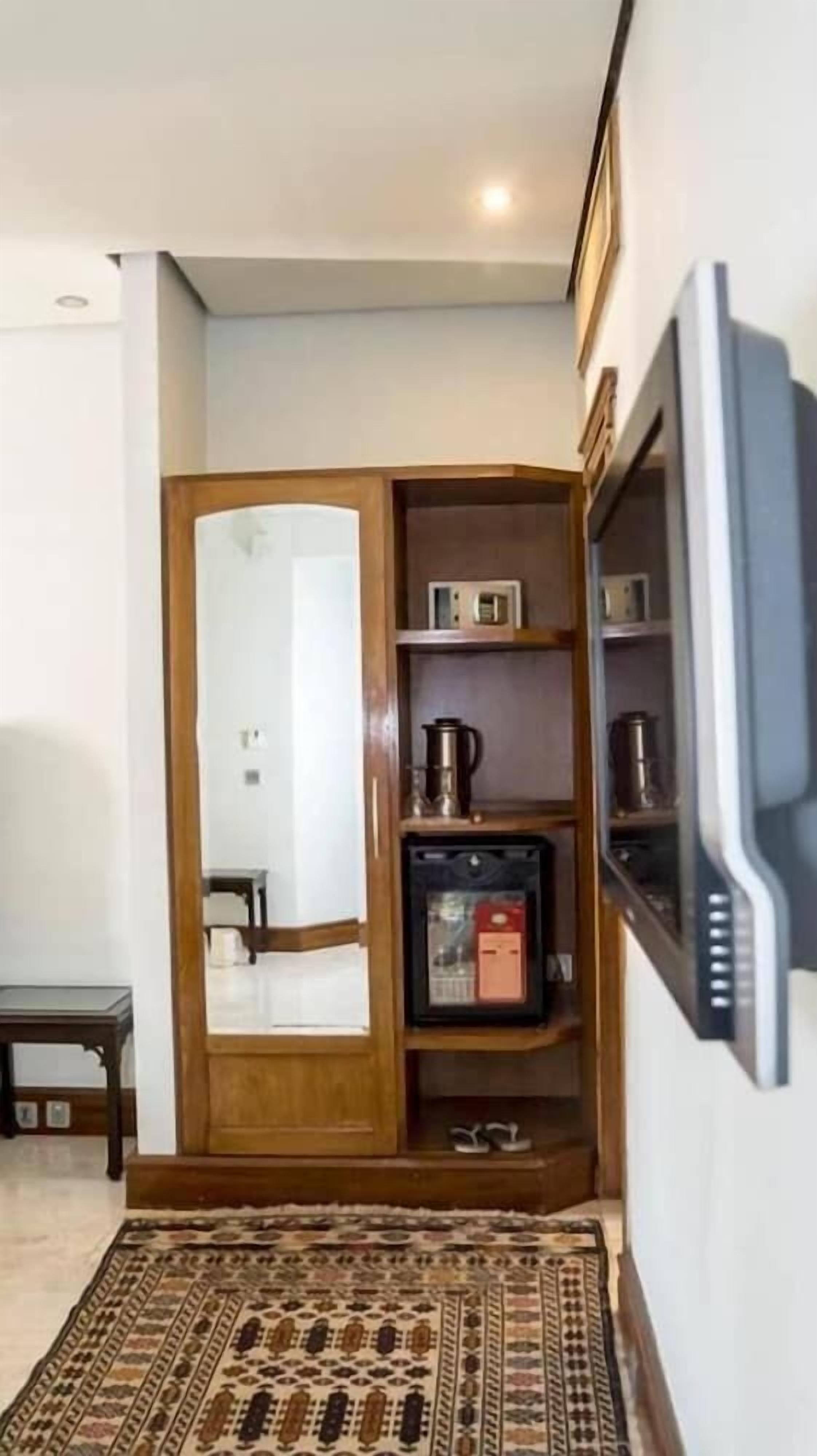 A compact living space with a wooden cabinet, a television mounted on the wall, and a patterned rug on the floor.