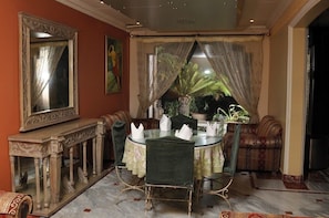 Un coin repas avec une table ronde, des chaises, un miroir et une vue sur un jardin à travers des rideaux légers.