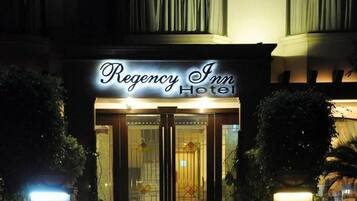 Exterior del Hotel Regency Inn con un llamativo letrero iluminado, entrada de vidrio y zona de acceso bien iluminada.