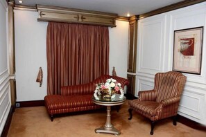 Una habitación con alfombra marrón, sofá rojo, sillón a rayas y una mesa con un arreglo floral.
