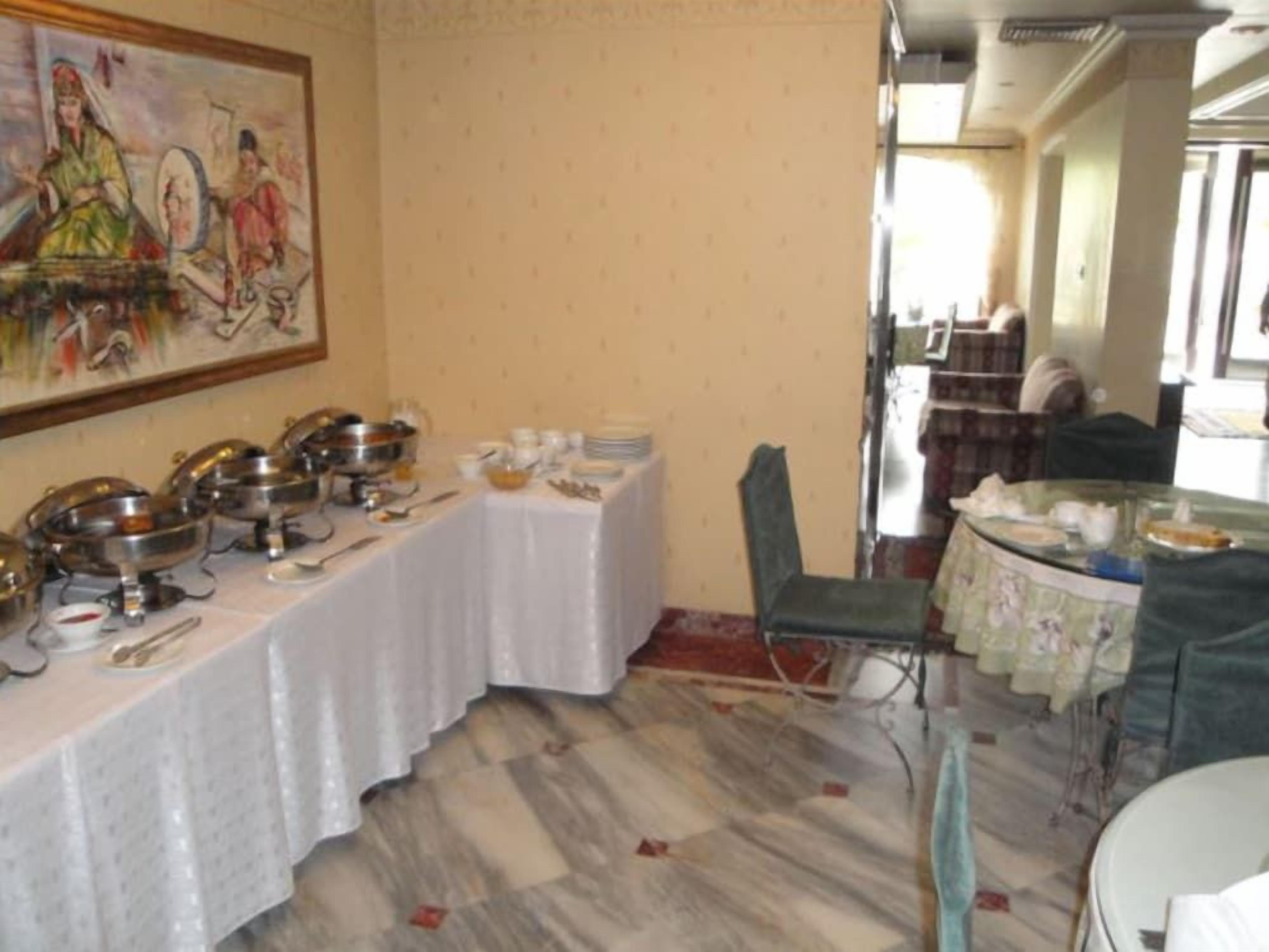 A dining area with a long table set for a meal, a painting on the wall, and a view of the outside.
