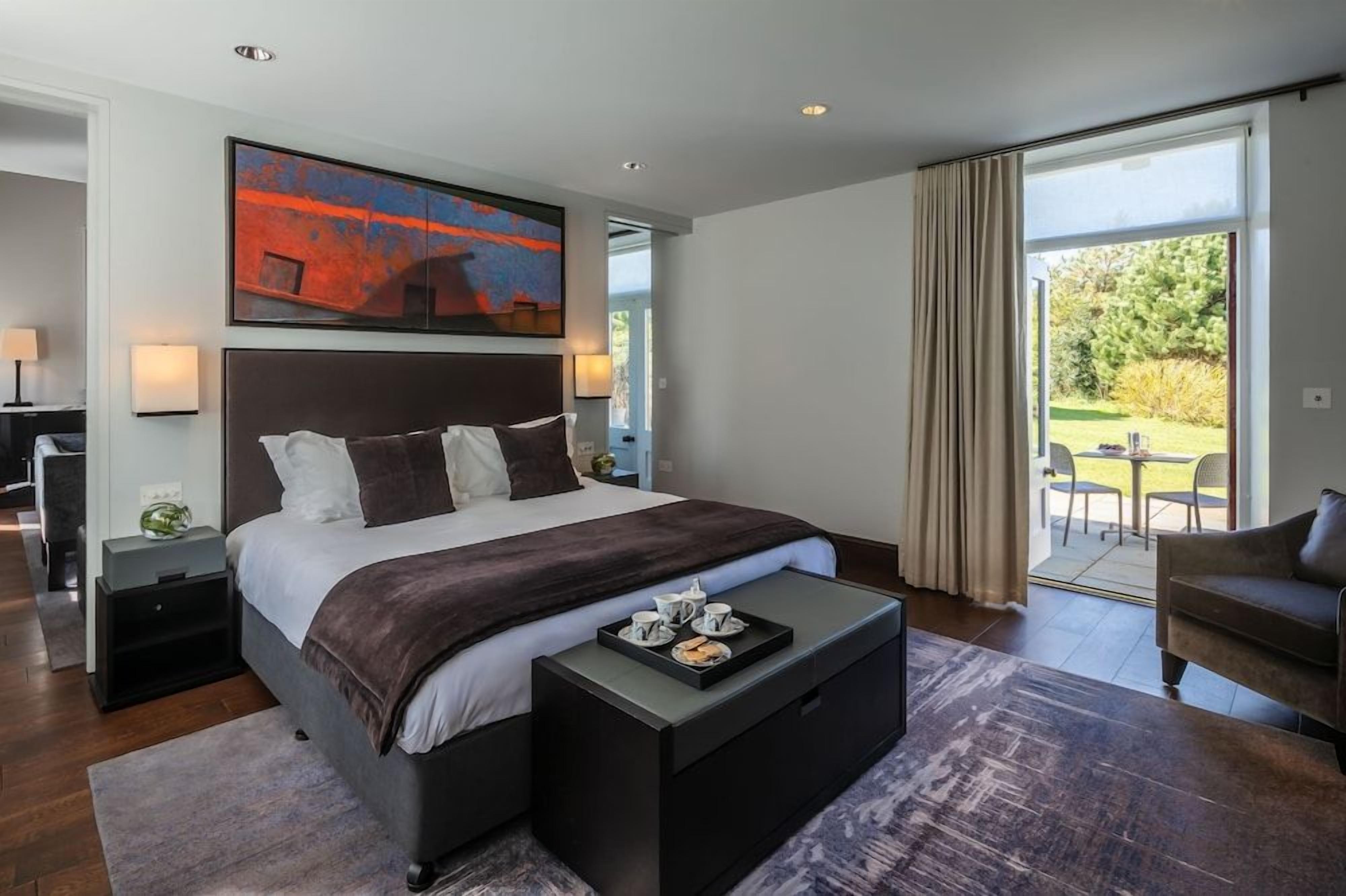 A modern bedroom with a large bed, a coffee table with breakfast items, and a view of the outdoors.
