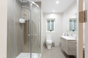 Un baño moderno con ducha envuelta en vidrio, inodoro y tocador con espejo.