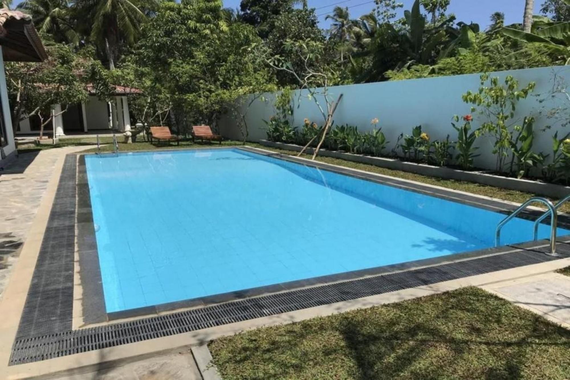 Una piscina rettangolare con una scaletta metallica su un lato, circondata da un solarium in cemento e un basso siepe.