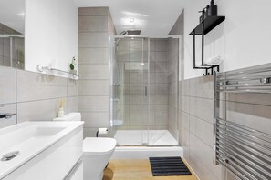 Et stilfuldt badeværelse med en brusekabine i glas, et hvidt badekar og et toilet.