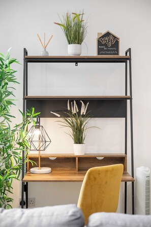 Een houten bureau met een gele stoel, een potplant, een decoratief bord en een geometrische lamp.