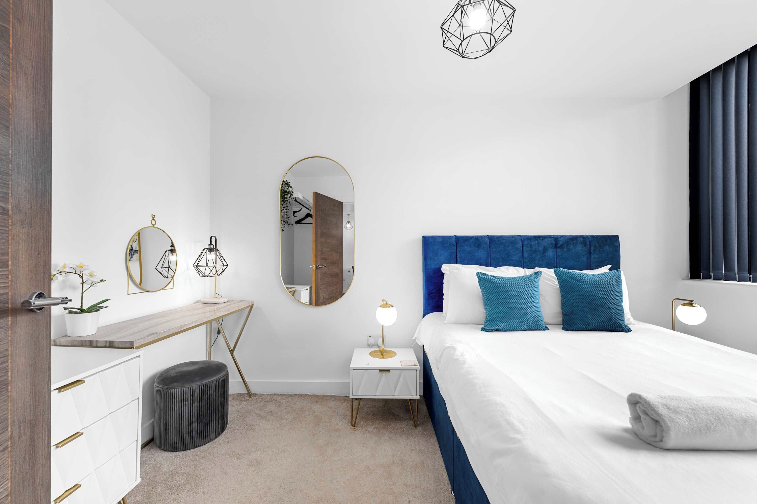Un dormitorio moderno con una cama grande, mesitas de noche, un escritorio y un espejo.
