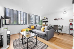 En moderne stue med en grå sofa, et glasbord og et stort vindue med lodrette skodder.
