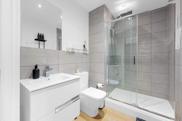 Een moderne badkamer met een douche met glazen wand, een witte wastafel en een toilet.