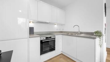Una cocina moderna con armarios blancos, horno empotrado, pileta de acero inoxidable y piso de madera.