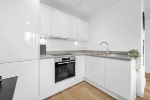 Een moderne keuken met witte kastjes, een inbouwoven, een RVS-gootsteen en een houten vloer.