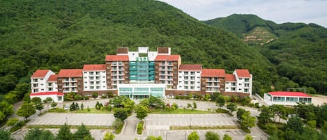 A multi-story hotel with a central courtyard, surrounded by lush greenery and hills.
