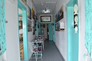 Un pasillo estrecho con puertas y paredes verde mar, un comedor con mesa y sillas, y varias obras de arte en las paredes.
