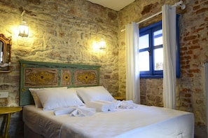Una habitación con pared de piedra, cama con ropa blanca y dos luces fijadas a la pared.