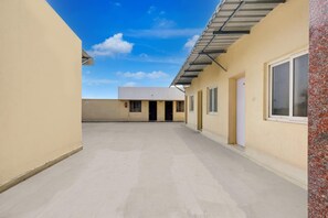 Ein Korridor mit zur Zimmer führenden Türen, einem strahlend blauen Himmel und einem Gebäude mit Flachdach.
