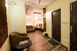A hotel room with a bed, a sofa, a small table, and a door with a marble finish. - Silver Arch Hotel (Dehradun)