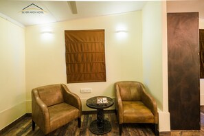 A hotel room with two leather armchairs, a small round table, and a brown curtain on the wall. - Silver Arch Hotel (Dehradun)