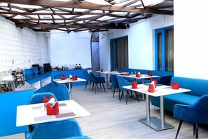 A restaurant with blue seating, white tables, and a kitchen area in the background. - Silver Arch Hotel (Dehradun)