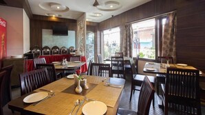 A restaurant with multiple dining tables, chairs, and a television mounted on the wall. - Chas Rajdarbar Hotel & Banquets (Siliguri)
