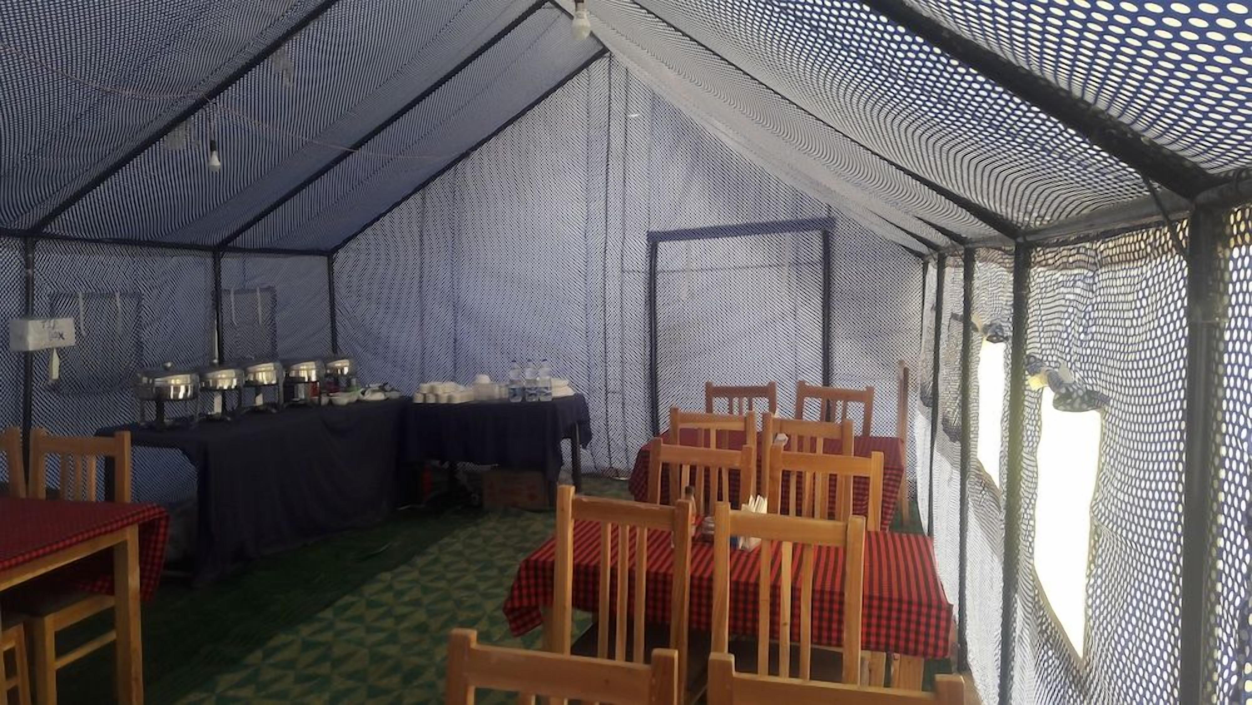 A tent with tables and chairs arranged inside, with a green patterned floor.
