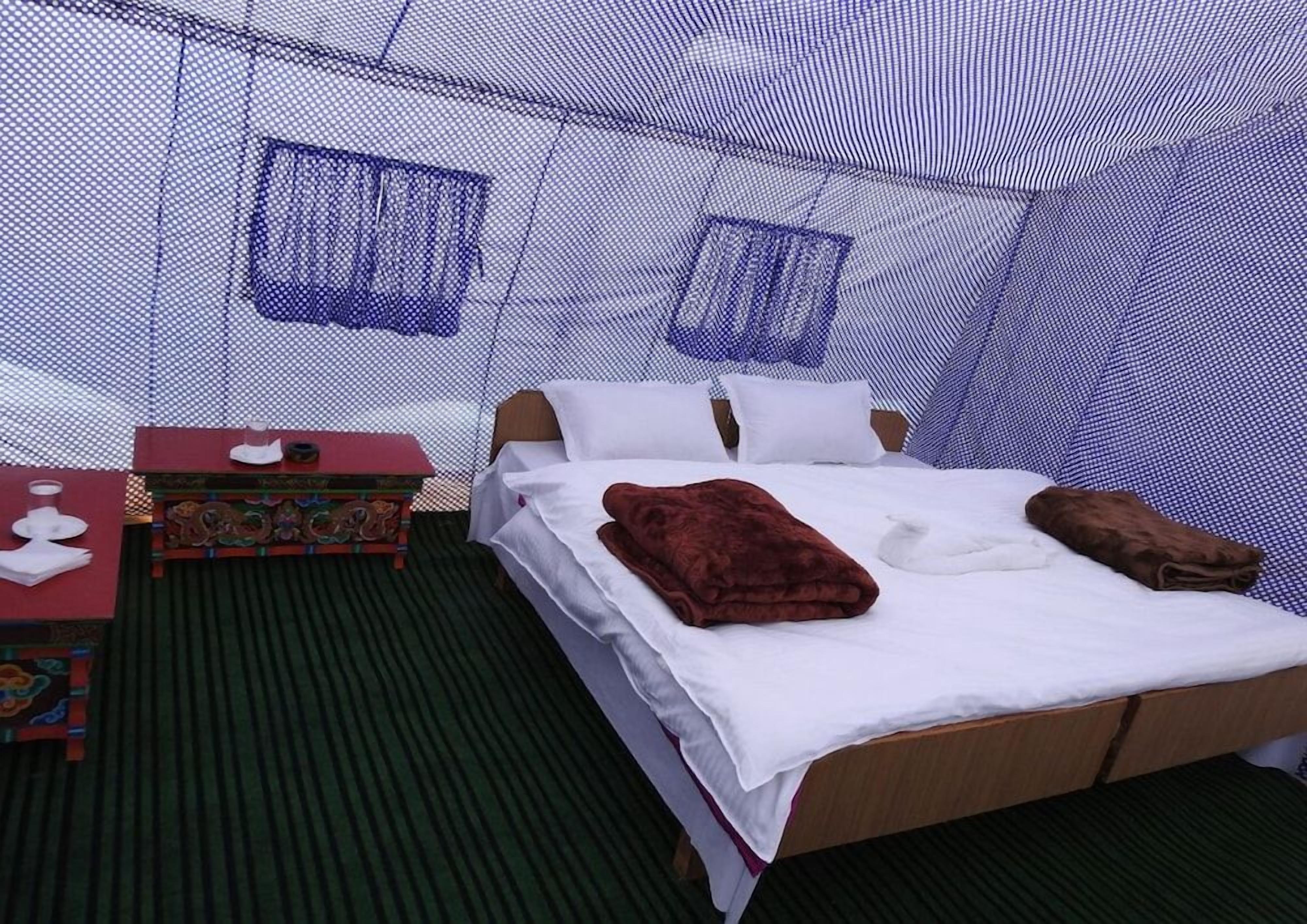 A single-bed room with a mosquito net, a small table with a decorative box, and a pair of slippers on the bed.