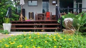 A covered outdoor area with a wooden deck, a chair, and a table. - Nan @ Pua (Pua)