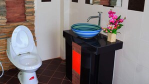 A bathroom with a toilet, a green bucket, a blue basin, and a pink flower arrangement. - Nan @ Pua (Pua)