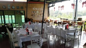 A restaurant with multiple tables set for dining, white chairs, and a view through large windows. - Nan @ Pua (Pua)