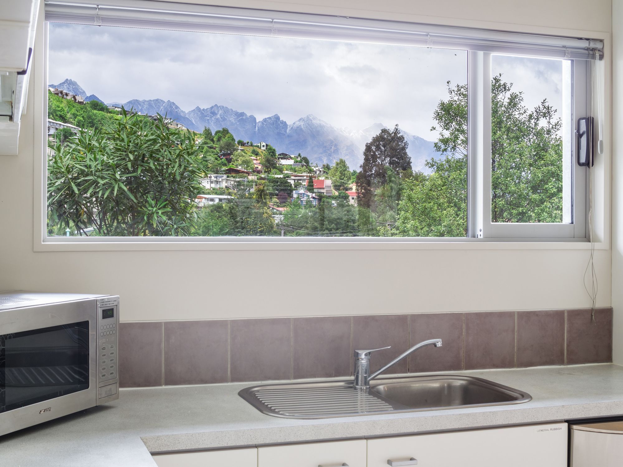 A kitchen with a built-in microwave, a sink, and a window offering a view of a mountainous landscape.