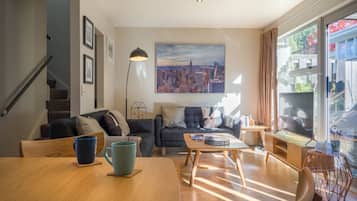 A modern living room with a wooden dining table, sofas, and a cityscape painting on the wall.