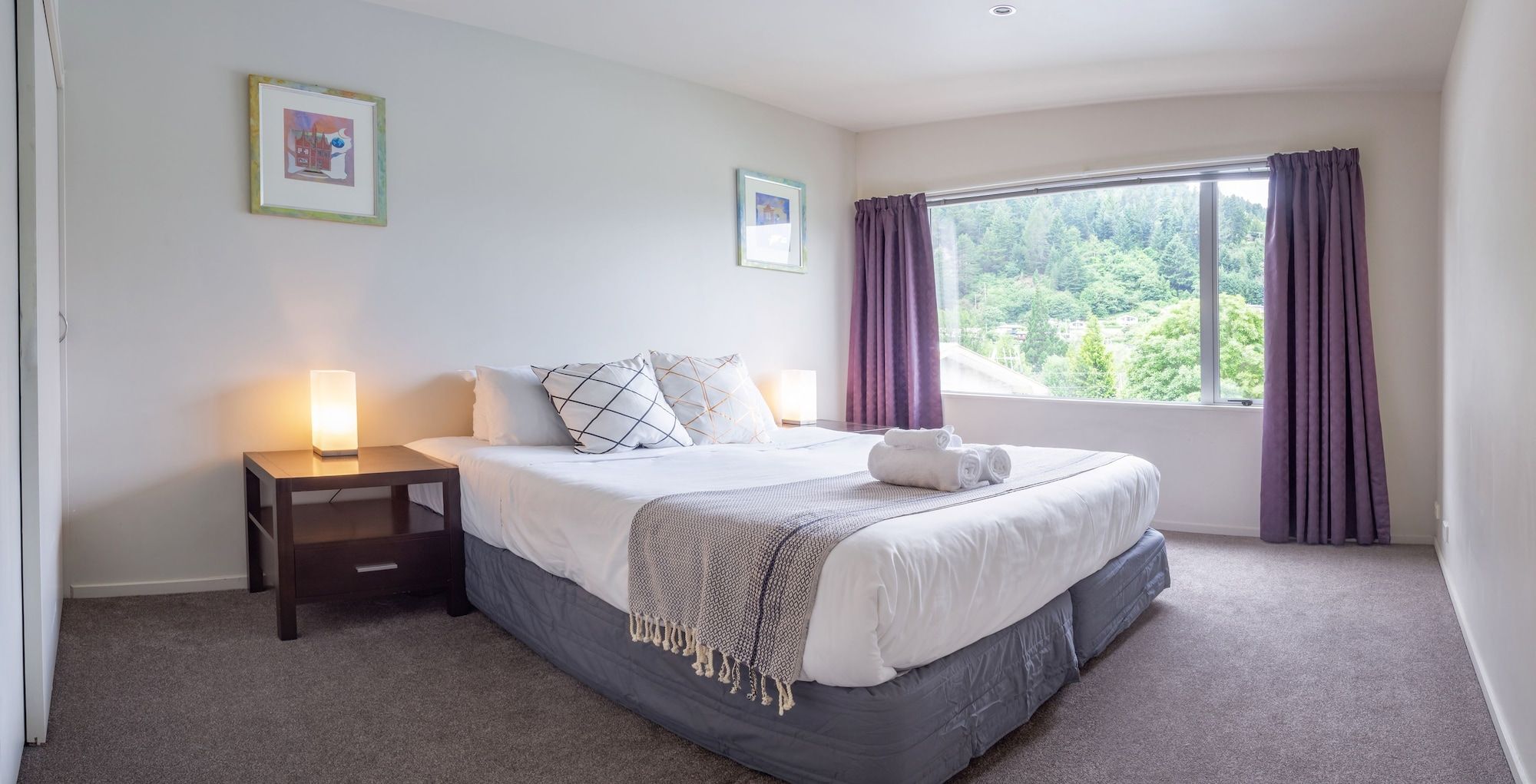 A bedroom with a bed, bedside lamps, a nightstand, and a window with curtains.