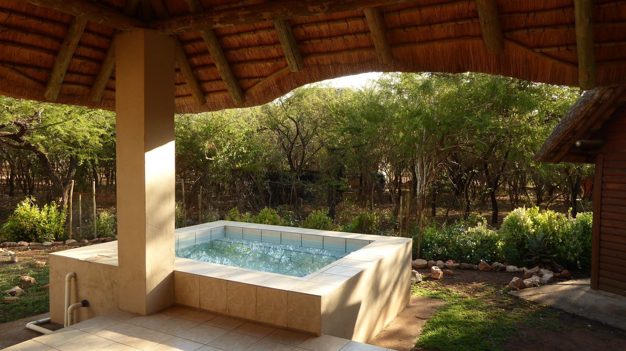 A hot tub under a wooden structure surrounded by greenery.