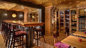 Un bar con mesas y sillas de madera, pared de ladrillo y estantes con botellas.