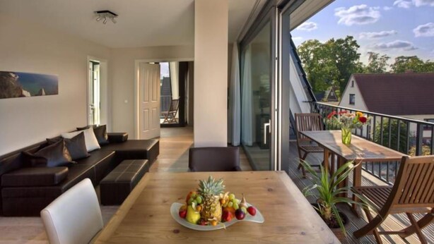 Una sala de estar moderna con una mesa de comedor de madera, un sofá y un balcón con vistas del entorno.