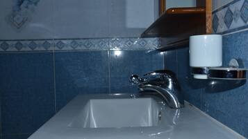 A bathroom sink with a chrome faucet, a white cup holder, and blue patterned tiles.